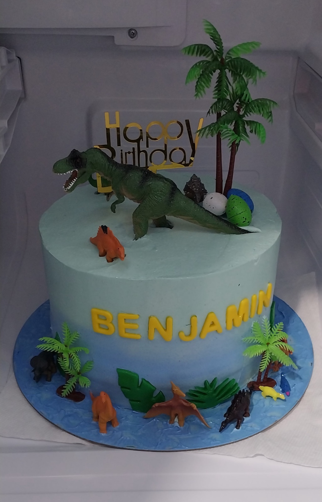 Blue dinosaur-themed birthday cake with palm trees